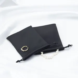 Vista detallada de bolsas de satén negro con cordón y accesorios para joyería