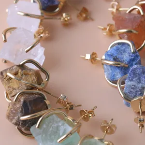 Macro view of irregular raw gemstone stud earrings with gold-plated four-claw settings.