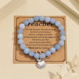 Macro detail of blue natural stone beaded bracelet with silver apple charm on gift card