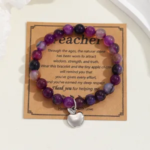 Detailed view of purple natural stone bead bracelet with silver apple charm on gift card