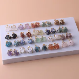 Collection of assorted raw crystal stud earrings in gold-plated settings on white slab