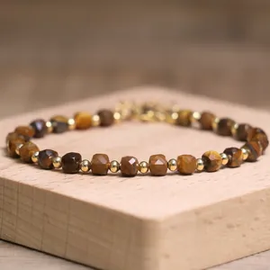 Macro detail of natural tiger eye stones and gold beads on a minimalist wooden stand