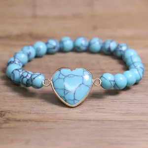 Detailed macro view of turquoise beaded bracelet with gold-framed heart center stone.