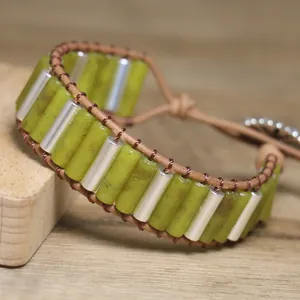 Close-up detail of olive green stone and metal tube woven wrap bracelet on wood.