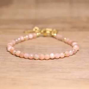 Detailed view of faceted natural peach stone beads on a gold adjustable bracelet.