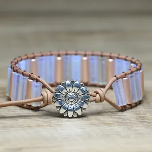 Detailed view of handmade opal stone woven bracelet with silver flower clasp on wood.