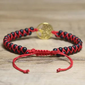 Close-up detail of a handmade red woven bracelet with black stones and a golden Tree of Life charm