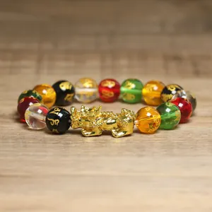Gros plan d'un bracelet en perles colorées avec un pendentif PiXiu doré et des mantras.