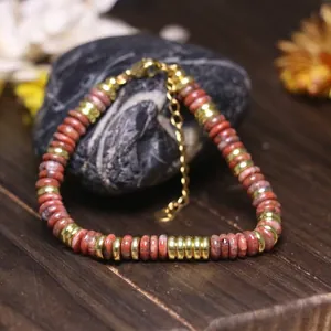 Dettaglio di perle in pietra rossa e distanziatori dorati in acciaio su bracciale regolabile
