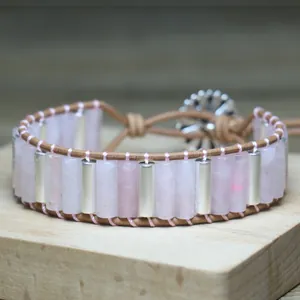 Detail of a hand-woven rose quartz bracelet with silver metal tubes on a wood base