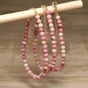 Detailed view of three pink natural stone beaded bracelets hanging on a wooden rod