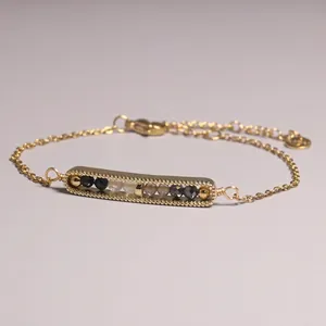 Close-up detail of a gold-plated bar bracelet featuring black beads and citrine stones.