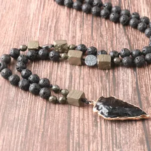 Detalle del colgante punta de flecha de obsidiana y cuentas de lava sobre madera.