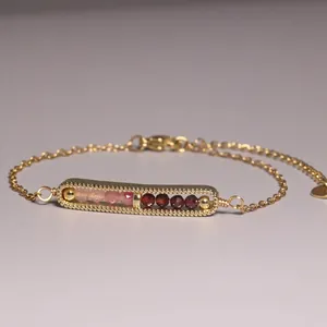 Detailed close-up of gold-plated chain bracelet with pink and dark red faceted stone beads