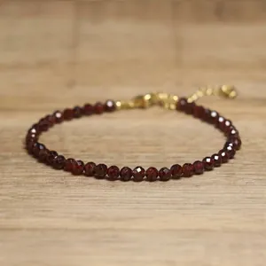 Detailed view of faceted dark red gemstone beads on an adjustable gold chain bracelet.