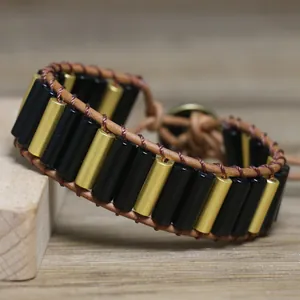 Macro detail of hand-woven bracelet with black and gold cylindrical beads on leather