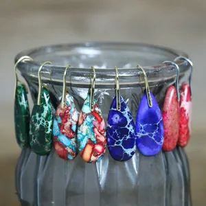 Close-up detail of colorful teardrop imperial stone earrings displayed on a glass vase rim