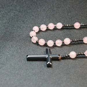 Detailopname van 8mm rozenkwartskralen en een zwarte kruishanger op grijze basis