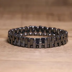 Close-up of a dark metallic hematite beaded stretch bracelet on a wooden surface.
