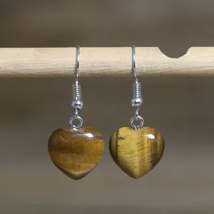 Detailed view of natural tiger eye stone heart-shaped earrings on wooden stick