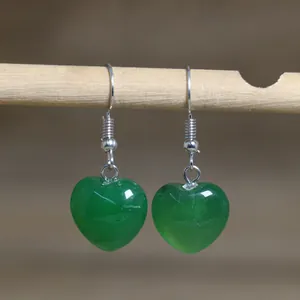 Detail showing green heart-shaped natural stone dangle earrings on wooden hanger