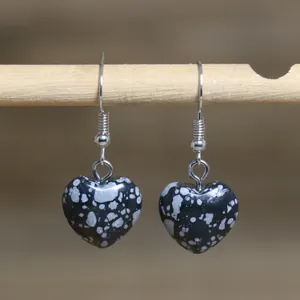 Macro detail of heart-shaped snowflake obsidian drop earrings hanging on a wooden rod.