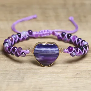 Nahaufnahme des lila Amethyst-Perlenarmbands mit Herzanhänger auf Holzuntergrund.