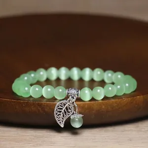 Macro view of green cat's eye stone bead bracelet featuring a silver leaf charm.