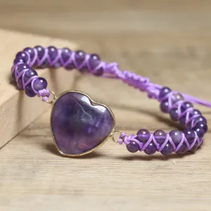 Nahaufnahme eines herzförmigen Amethyststeins an einem lila geflochtenen, verstellbaren Armband.