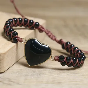 Detailaufnahme eines schwarzen Herzstein-Anhängers an einem braun geflochtenen Perlenarmband.