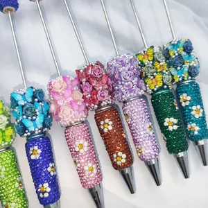 Close-up of luxury rhinestone ballpoint pens with 3D butterfly and rose decorations.