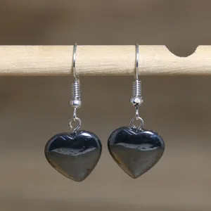 Detail shot of heart-shaped natural stone earrings hanging on a light wooden bar.