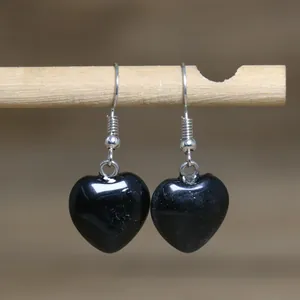 Close-up of elegant black natural stone heart drop earrings hanging from a wooden stick
