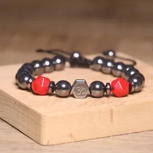 Detailopname van hematiet armband met rode kralen en een spiritueel Om-symbool bedeltje.