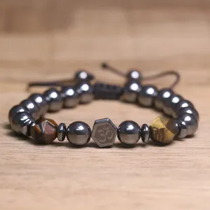 Macro-opname van een gevlochten hematiet armband met centraal Om-symbool en tijgeroog