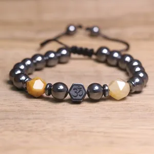 Detailopname van een hematiet kralenarmband met geslepen stenen en een Om-symbool.