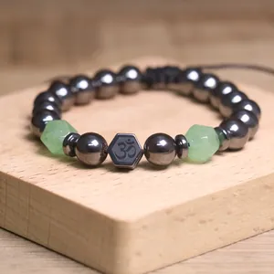 Detailopname van hematiet kralenarmband met groene stenen en Om-symbool op hout.