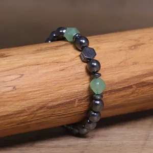 Close-up van hematiet kralenarmband met groene stenen en een Om-symbool kraal.