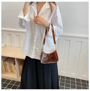 Modieuze bruine transparante PVC baguette tas onder de arm getoond op een model.