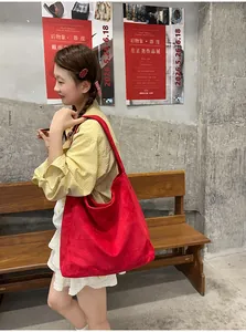 Femme élégante en chemise jaune portant un grand cabas en daim rouge dans un décor de studio urbain