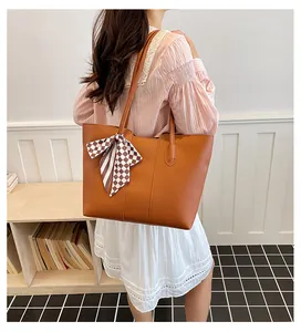 Elegante bruine leren draagtas met een geruite zijden sjaal, getoond op een schouder.