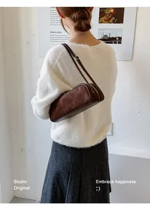 Brown suede baguette bag worn on shoulder with white sweater and grey skirt.