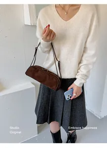 Woman holding a brown suede baguette bag with cream sweater and grey skirt.