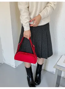 Model holding a vibrant red suede baguette bag styled with a grey pleated skirt