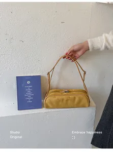 Mustard suede bowling bag held by hand against a minimalist white backdrop
