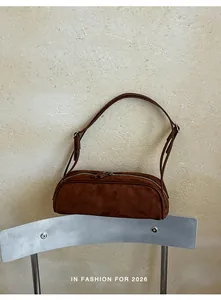 Detailed view of a minimalist brown suede baguette bag resting on a metal chair
