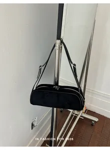 Side view of a minimalist black suede baguette bowling bag hanging on a metal stand