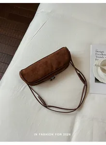 Elegant brown suede baguette bag with shoulder strap on a white minimalist bedsheet