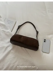 Brown suede bowling baguette bag for women lying on a minimalist white fabric background.