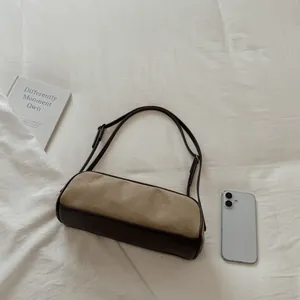 Minimalist khaki suede bowling bag with dark brown leather trim shown on white fabric